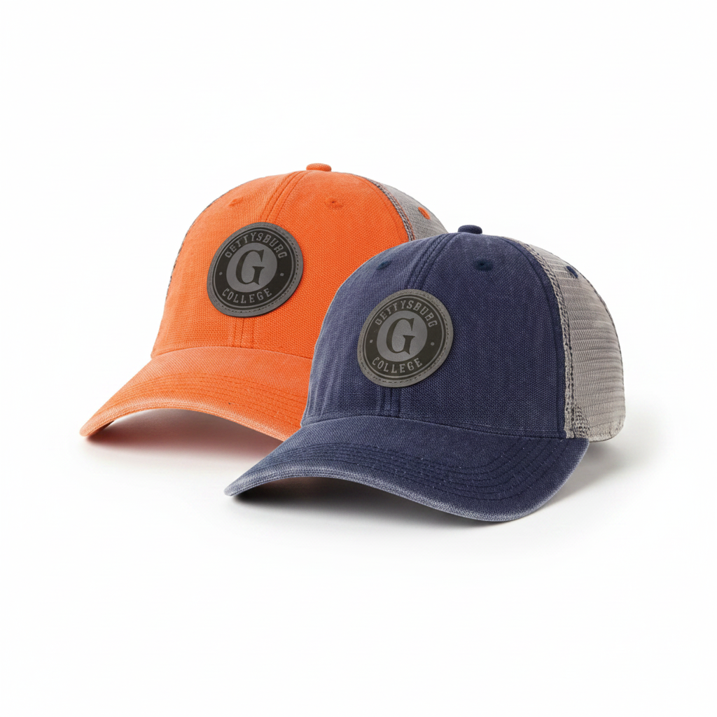 Two baseball caps shown on a plain white background: one bright orange cap in back and one navy blue cap in front. Both caps have circular dark gray patches on the front with a large letter G and the words 'Gettysburg College'